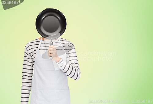 Image of man or cook in apron hiding face behind frying pan