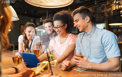 Image of happy friends with tablet pc and drinks at bar