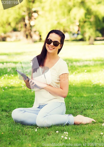 Image of smiling young girl with tablet pc sitting on grass