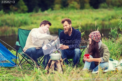 Image of group of smiling tourists cooking food in camping