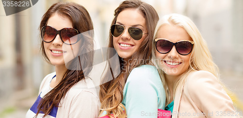 Image of three smiling women in sunglasses with bags