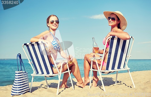 Image of happy women sunbathing in lounges on beach