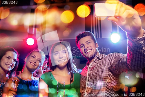 Image of friends taking selfie by smartphone in night club