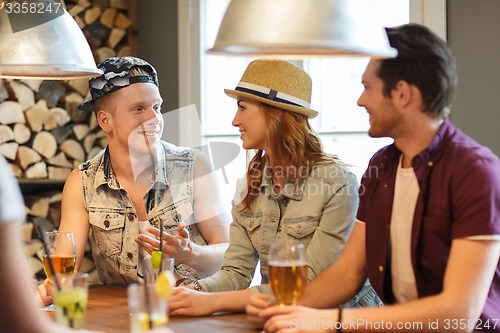 Image of happy friends drinking beer and cocktails at bar