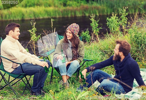 Image of group of smiling tourists drinking beer in camping