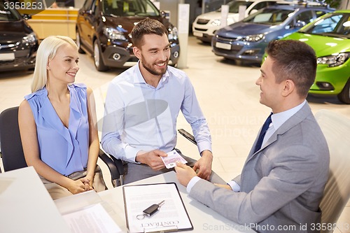 Image of happy couple with car dealer in auto show or salon