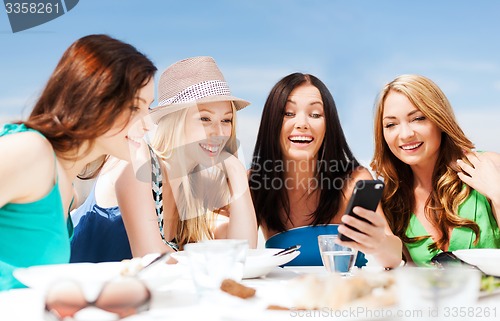 Image of girls looking at smartphone in cafe on the beach