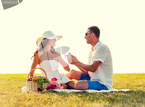 Image of smiling couple with small red gift box on picnic