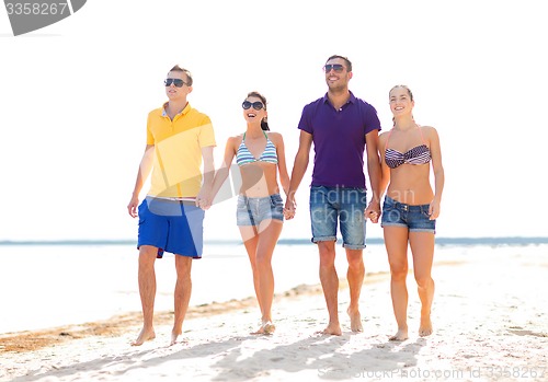 Image of group of happy friends walking along beach