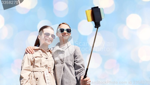 Image of happy girls with smartphone selfie stick over blue