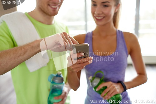 Image of happy woman and trainer showing smartphone in gym