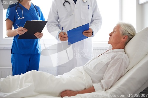 Image of doctor and nurse visiting senior woman at hospital