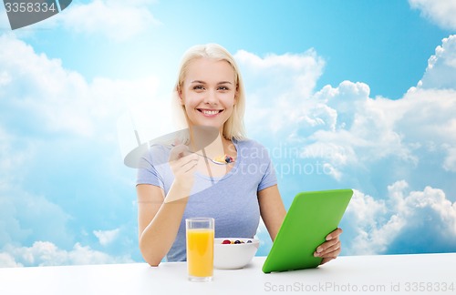 Image of smiling woman with tablet pc eating breakfast