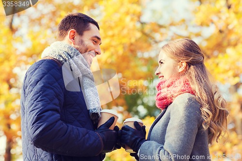 Image of smiling couple with coffee cups in autumn park