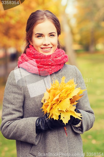 Image of smiling woman with bunch of leaves in autumn park
