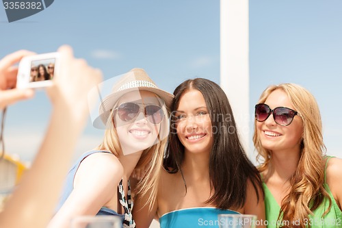 Image of girls taking photo with digital camera in cafe