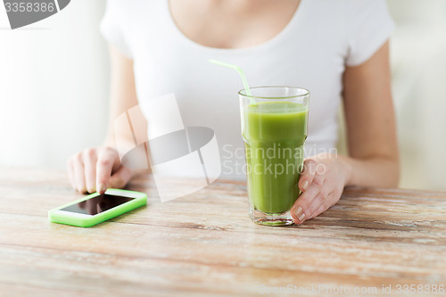 Image of close up of woman with smartphone and green juice