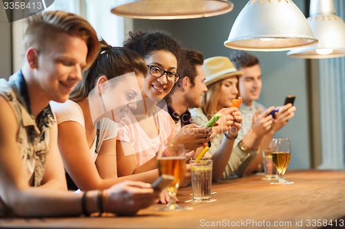 Image of happy friends with smartphones and drinks at bar