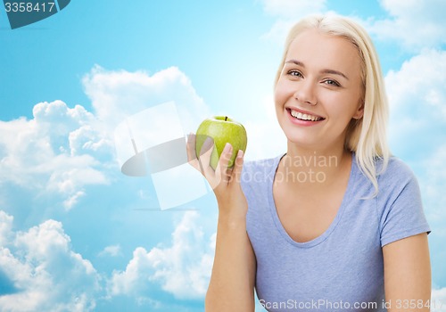 Image of happy woman eating green apple over sky