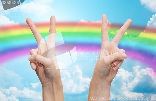 Image of hands showing peace sign over rainbow in sky