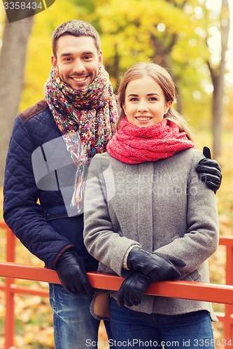 Image of smiling couple hugging on bridge in autumn park