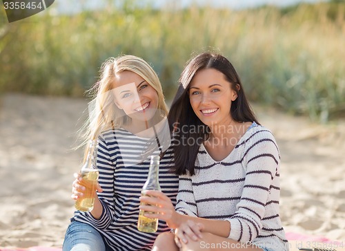 Image of happy young women drinking beer on beach