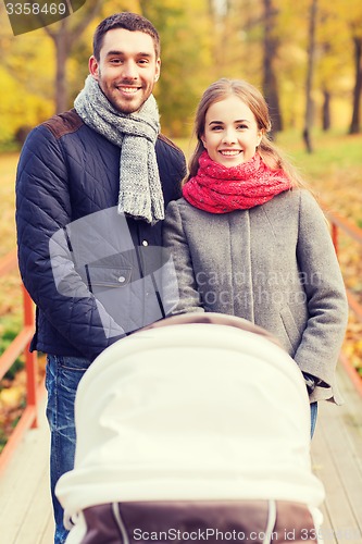 Image of smiling couple with baby pram in autumn park