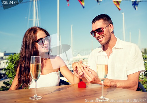 Image of smiling couple with champagne and gift at cafe