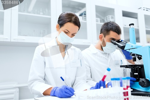 Image of scientists with clipboard and microscope in lab