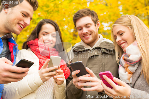 Image of smiling friends with smartphones in autumn park