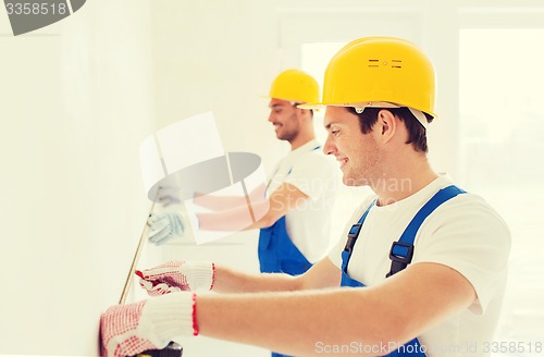 Image of smiling builders with measuring tape indoors