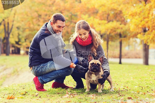 Image of smiling couple with dog in autumn park