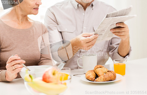 Image of happy senior couple reading newspaper at breakfast