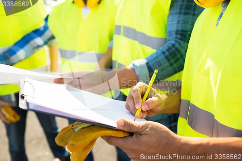 Image of close up of builders in vests writing to clipboard