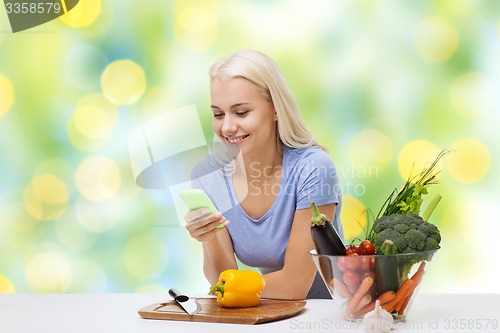 Image of smiling woman with smartphone cooking vegetables