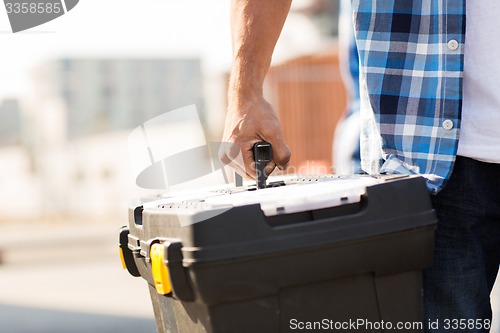 Image of close up of builder carrying toolbox outdoors