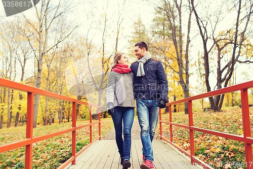 Image of smiling couple hugging on bridge in autumn park