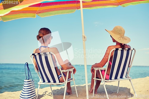 Image of happy women sunbathing in lounges on beach