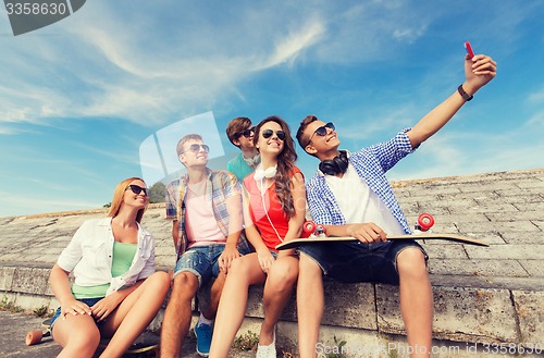 Image of group of smiling friends with smartphone outdoors