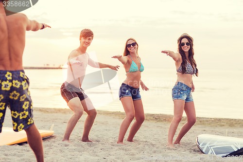 Image of smiling friends in sunglasses with surfs on beach