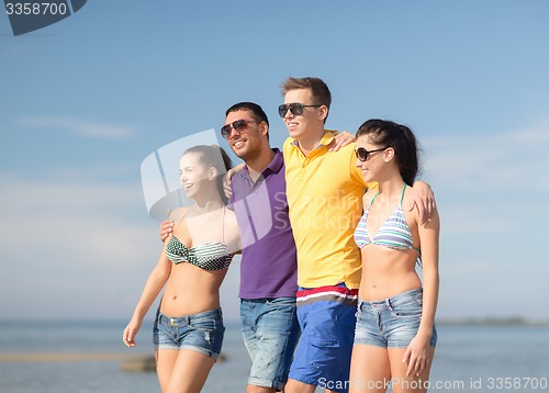 Image of group of happy friends walking along beach