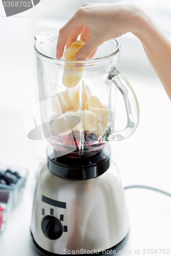 Image of close up of woman hand adding fruits to blender