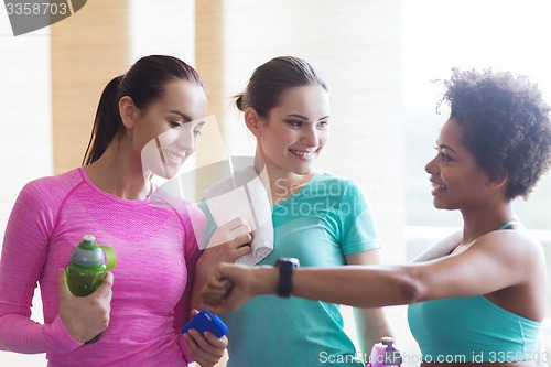 Image of happy women showing time on wrist watch in gym