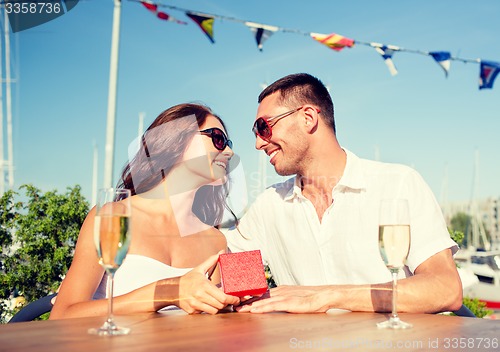 Image of smiling couple with champagne and gift at cafe