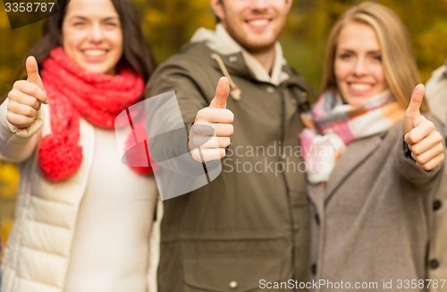 Image of happy friends showing thumbs up in autumn park