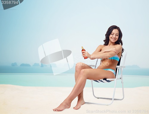 Image of happy woman sunbathing and applying sunscreen