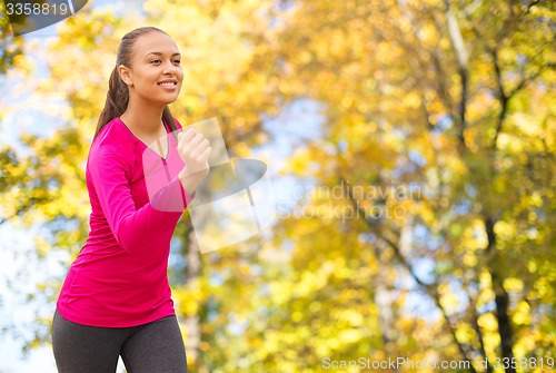 Image of smiling woman running outdoors at autumn