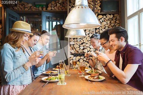 Image of happy friends with smartphones picturing food