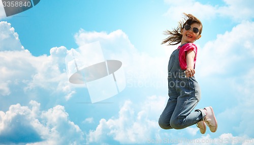 Image of happy little girl jumping high over blue sky