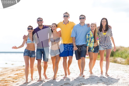Image of group of happy friends walking along beach